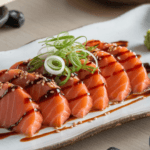 Soy sauce-marinated raw salmon slices garnished with green onions and sesame seeds on a white plate