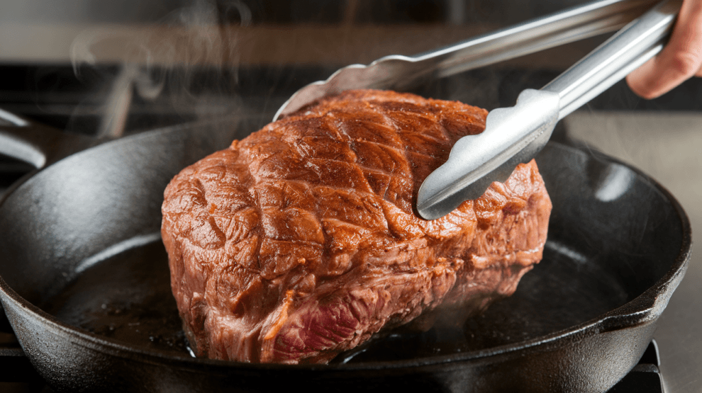 Searing a sous vide prime rib in a cast iron skillet to create a golden-brown crust, with steam and oil droplets highlighting the process

